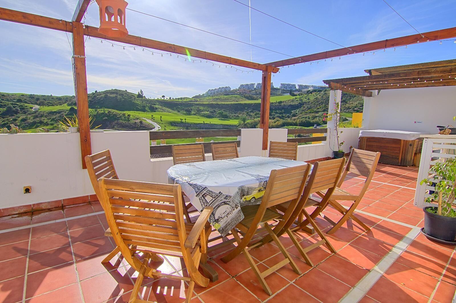 A terrace with a table and chairs, a pergola, and a view of green hills.