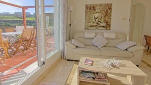 Una sala de estar con un sofá, una mesa de centro y vistas a una terraza con mesa y sillas.