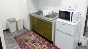 Ett kompakt kök med mikrovågsugn, diskho och ett litet kylskåp. Det finns två papperskorgar och en mönstrad matta på golvet.