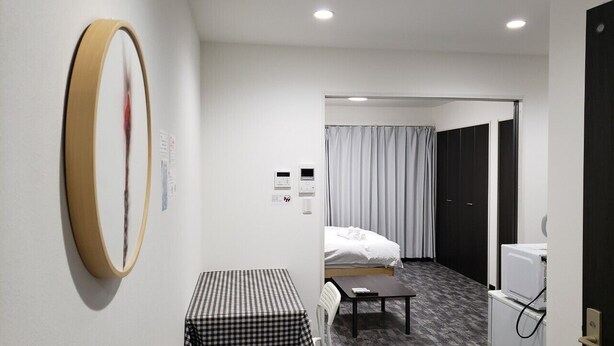 Ett hotellrum med en säng, ett litet bord, en stol, en tvättmaskin och en stor spegel på väggen.