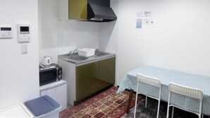 Ett litet, praktiskt kök med mikrovågsugn, vattenkokare och ett litet kylskåp. Här finns också en diskho med ett diskställ, ett bord med stolar och en mönstrad matta.