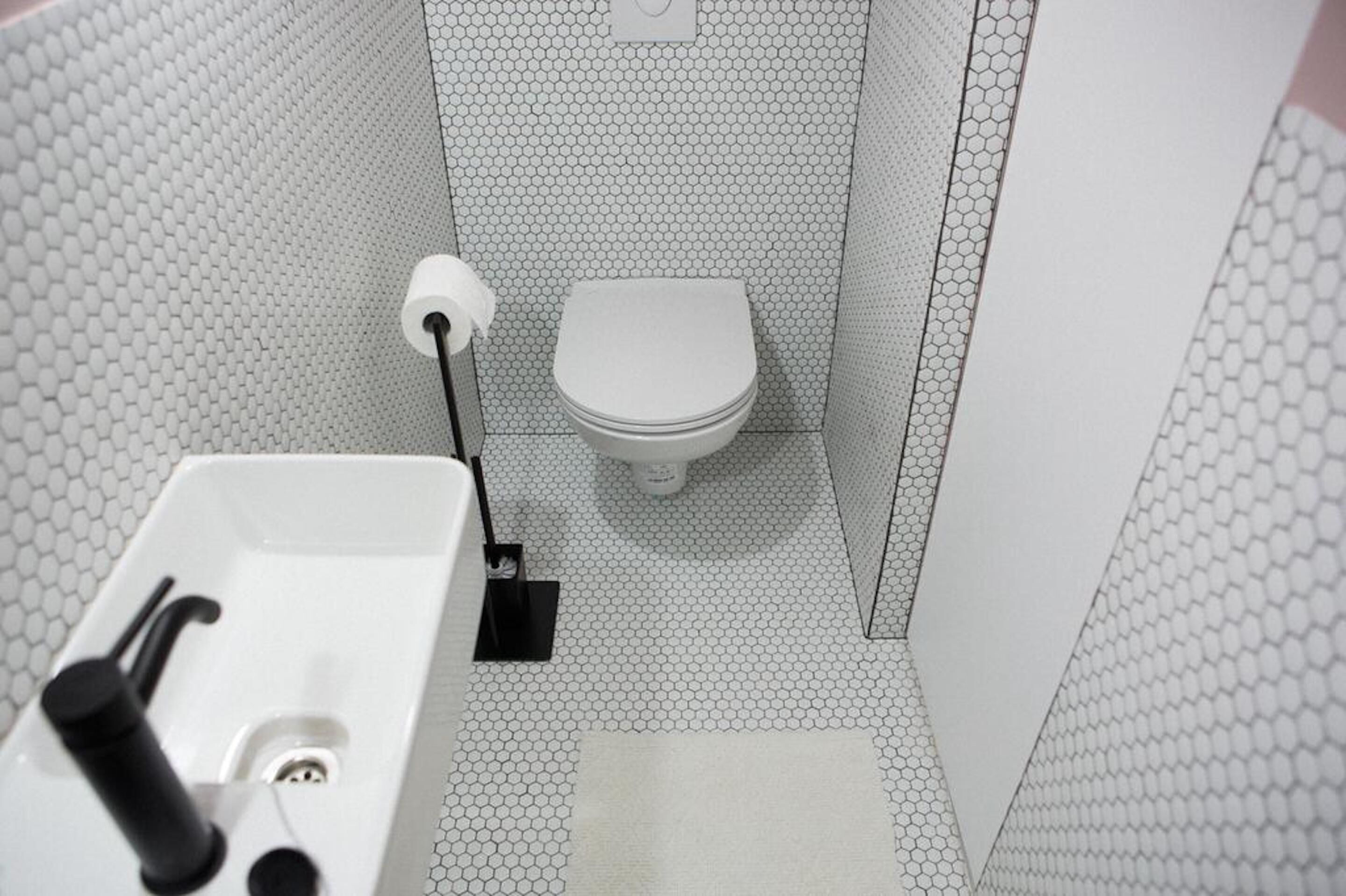 Un baño con inodoro blanco, lavamanos con grifo negro y dispensador de papel higiénico en la pared.
