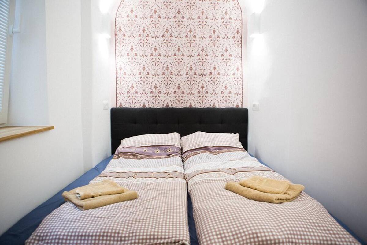 A double bed with a patterned headboard, two towels, and a checkered bedspread.