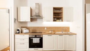 A modern kitchen with white cabinets, a stainless steel range hood, a built-in oven, and a sink. - Codelli Deluxe Unique Fresko Apartments (Ljubljana)
