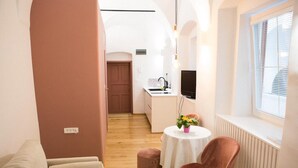 A cozy living area with a sofa, a round table with a vase of flowers, a pink chair, and a television. - Codelli Deluxe Unique Fresko Apartments (Ljubljana)