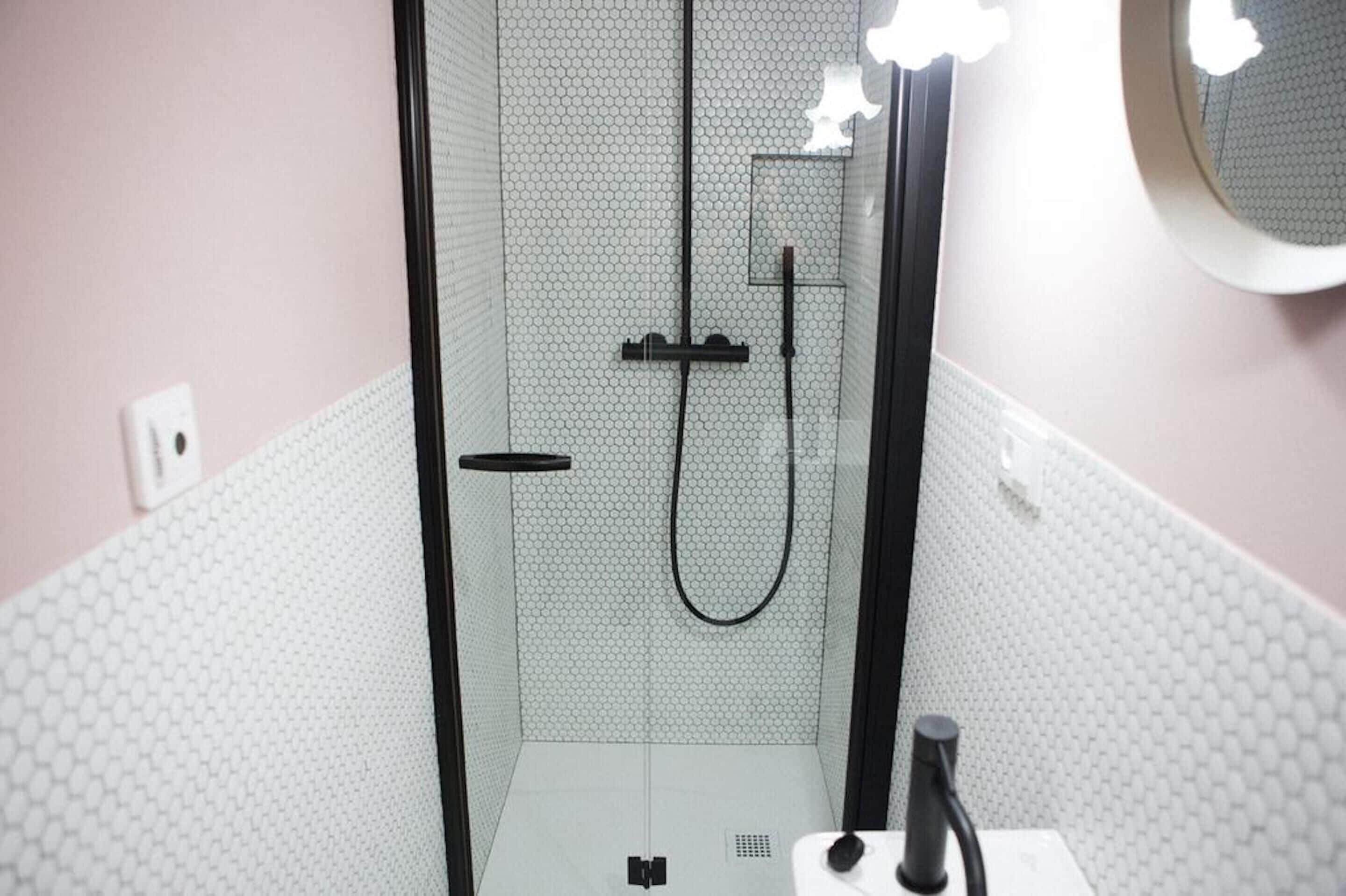 A bathroom with a glass-enclosed shower, a white tiled wall, and a round mirror.