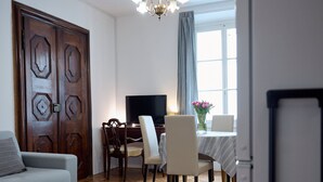 A living room with a sofa, a dining table with chairs, a TV, and a chandelier. - Codelli Deluxe Unique Fresko Apartments (Ljubljana)