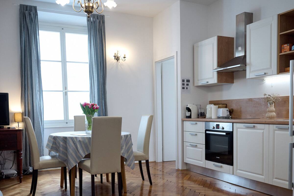 A modern kitchen with white cabinets, a built-in oven, and a dining area with a table and chairs.