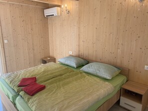 A wooden-paneled room with a bed, pillows, a nightstand, and an air conditioning unit.