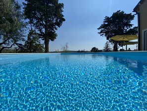 A clear blue pool with a view of trees and a building in the background. - Villa Olive Oasis (Piran)
