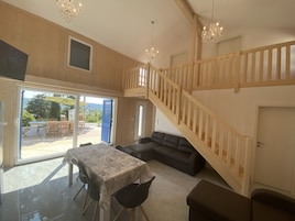 A spacious living area with a wooden staircase, a dining table with chairs, and a black sofa.