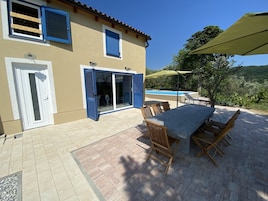 A patio with a table and chairs, a pool, and a building with blue shutters.