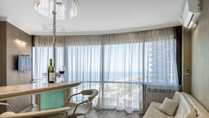A modern living room with a large window, a sofa, a dining area with chairs, and a bar. - Orbi Sea Towers Hotel Official (Batumi)