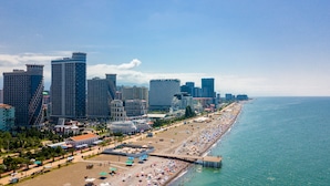A coastal cityscape with a long beach lined with palm trees and beach umbrellas. - Orbi Sea Towers Hotel Official (Batumi)