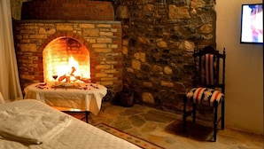 Une pièce chaleureuse avec une cheminée en pierre, un lit, un fauteuil agrémenté de coussins à motifs et un téléviseur fixé au mur.