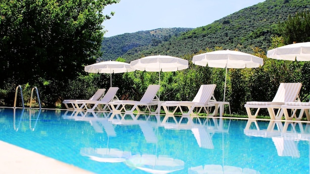 Une piscine bordée de chaises longues blanches et d’ombrelles, entourée d’une végétation luxuriante et avec des collines en arrière-plan.