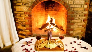 Une cheminée en pierre avec un feu, une table sur laquelle sont disposés un assortiment de fromages et des verres à vin, et une bougie.