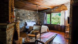 Une pièce chaleureuse avec une cheminée en pierre, un lit, un fauteuil et une vue sur la verdure.