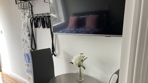 A compact room with a bed, a small round table with a vase of flowers, a chair, and a bench.