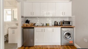 A compact kitchen with white cabinets, a sink, a dishwasher, a microwave, and a washing machine.