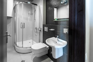 A modern bathroom with a glass-enclosed shower, a white toilet, and a pedestal sink.