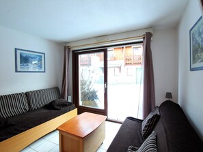 Un salon avec un canapé, une table basse en bois et une vue sur un immeuble par une grande fenêtre.
