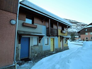 Un immeuble à plusieurs étages doté d’un balcon en bois, d’une porte bleue et d’une porte jaune.