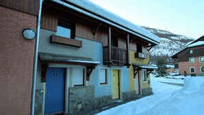 A multi-story building with a wooden balcony, a blue door, and a yellow door.