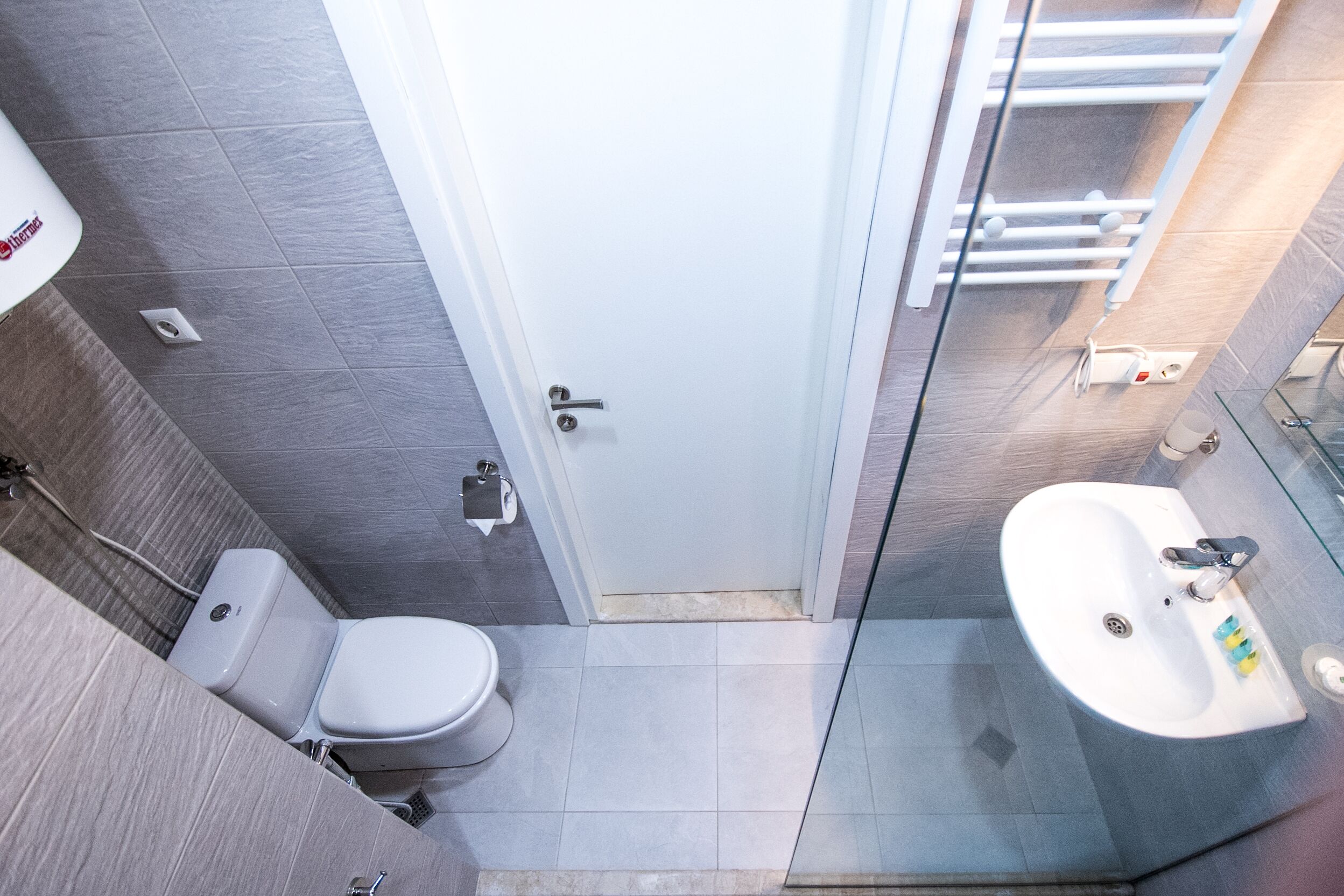 Un baño moderno con inodoro, lavamanos y cabina de ducha con mampara de vidrio.