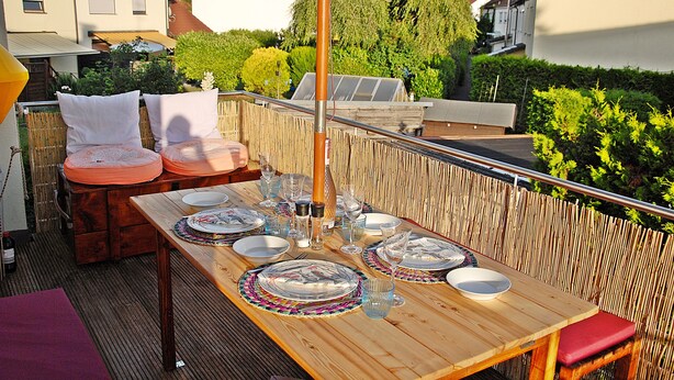 An outdoor dining area with a wooden table set for four, surrounded by a bamboo fence. - Sunny 4 room apartment near the lake with south-facing roof terrace
 (Eriskirch)