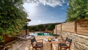 Um pátio de pedra com piscina, cadeiras de madeira e uma mesa posta para refeições.