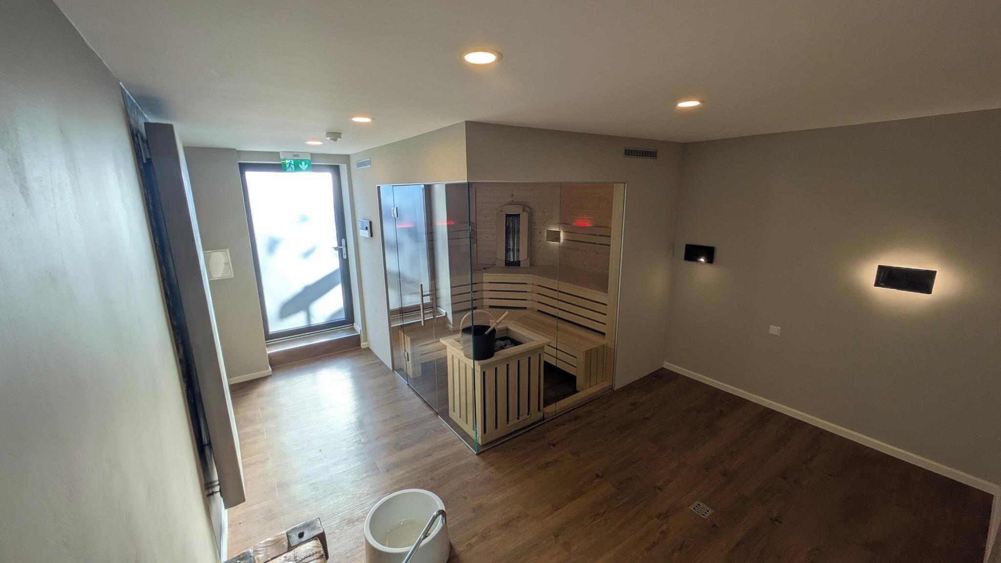 Un interior moderno con sauna, piso de madera y puerta de vidrio que da al exterior.