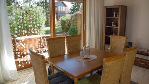 A dining area with a wooden table and wicker chairs, a glass pitcher, and a view of a garden through a glass door. - Ferienwohnung im Landhotel Sonneneck (Breuna)