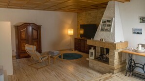 A living room with a stone fireplace, wooden furniture, and a television. - Ferienwohnung im Landhotel Sonneneck (Breuna)