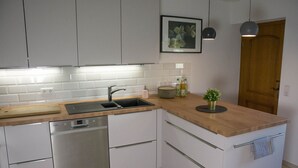 A modern kitchen with white cabinets, a dishwasher, a sink, and a wooden countertop. There is a potted plant on the countertop and a framed picture on the wall. - Ferienwohnung im Landhotel Sonneneck (Breuna)
