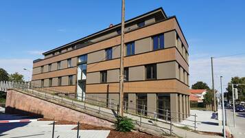 A modern multi-story building with a brick facade, large windows, and a pedestrian bridge leading to the entrance.