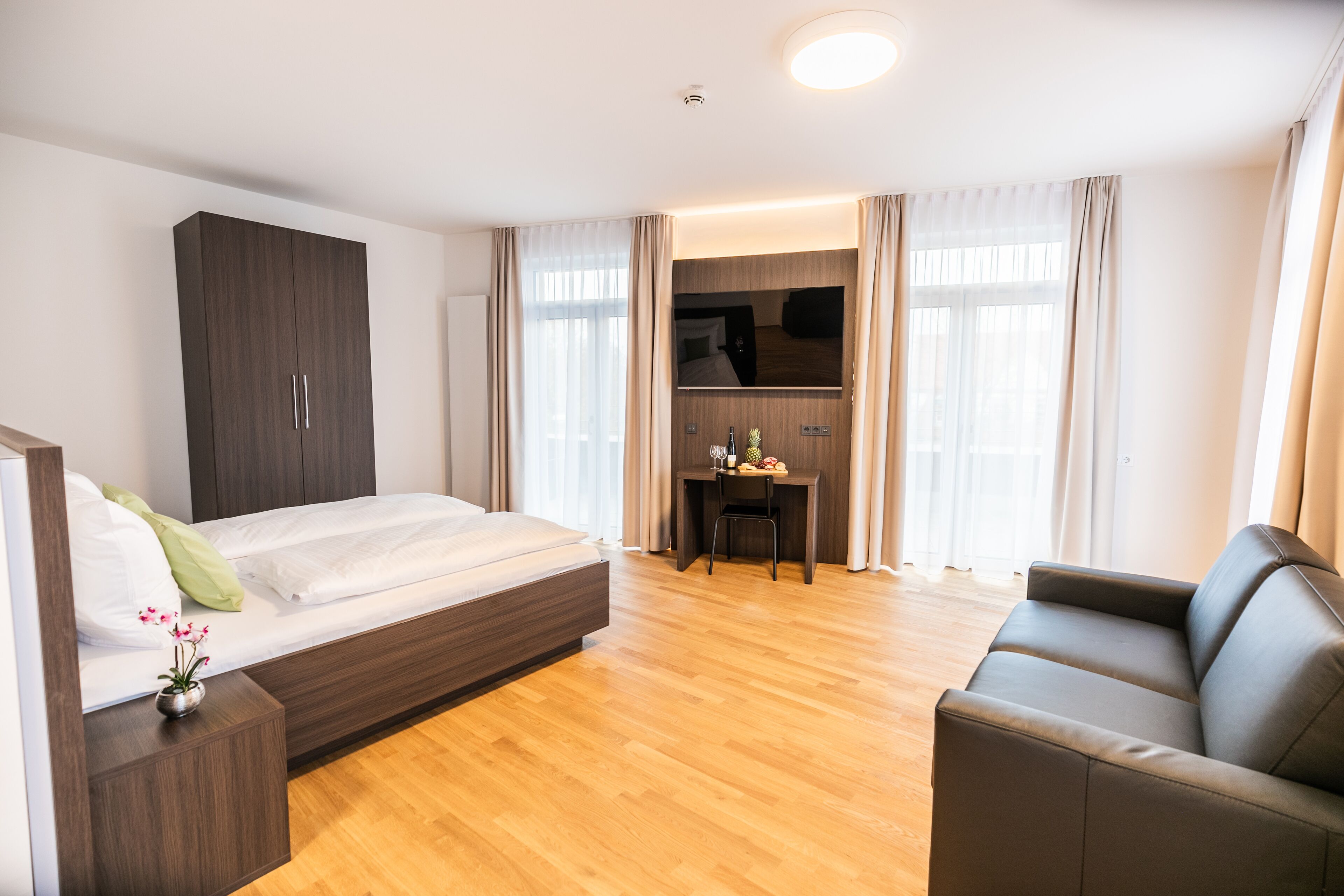 A modern hotel room with a bed, a desk, a sofa, and a TV.