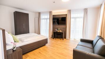 A modern hotel room with a bed, a desk, a sofa, and a TV.