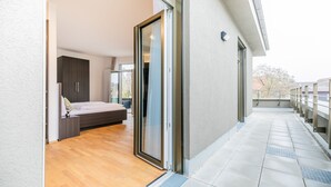 Un apartamento moderno con suelo de madera, una cama, un vidrio corredero y un balcón con barandilla.