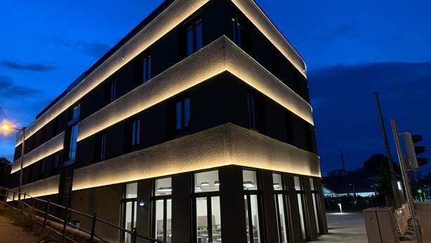 Un edificio moderno con un diseño angular único, grandes ventanas y una fachada bien iluminada.