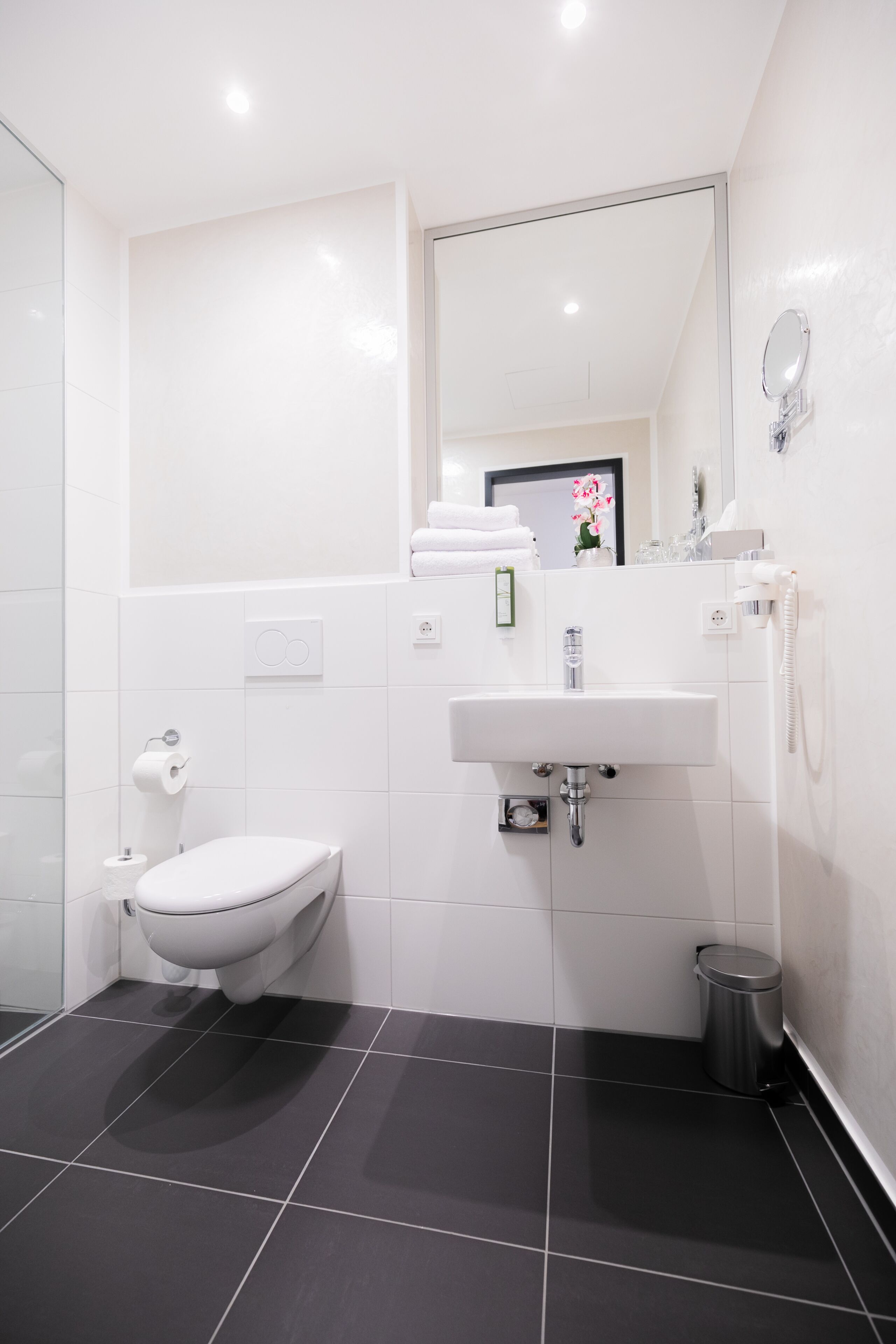 Un baño moderno con inodoro, lavamanos, espejo y un cesto de basura.