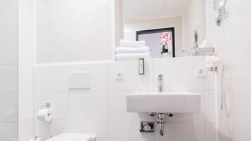 Un baño moderno con inodoro, lavamanos, espejo y un cesto de basura.