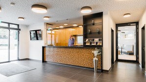 Un área de recepción moderna con una pared de mosaico de madera, un mostrador de recepción y un espacio de descanso visible a través de una puerta de cristal.