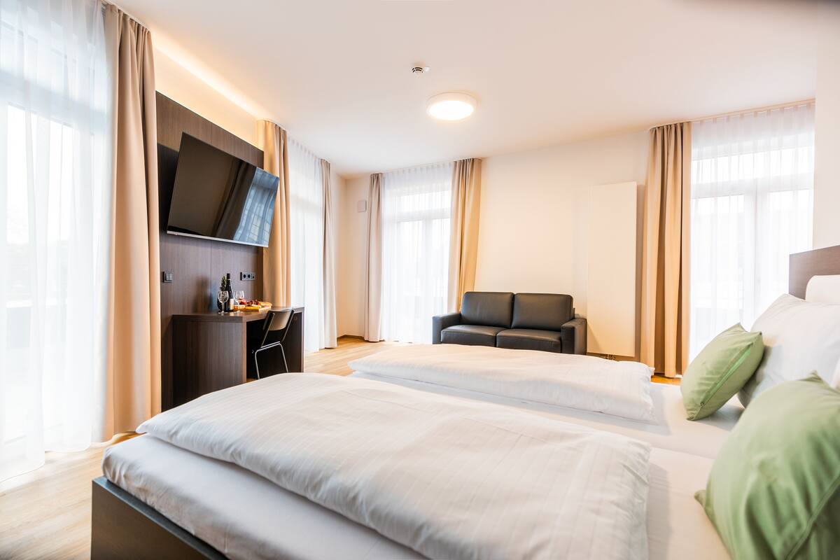 A hotel room with two beds, a desk, a TV, and a sofa.