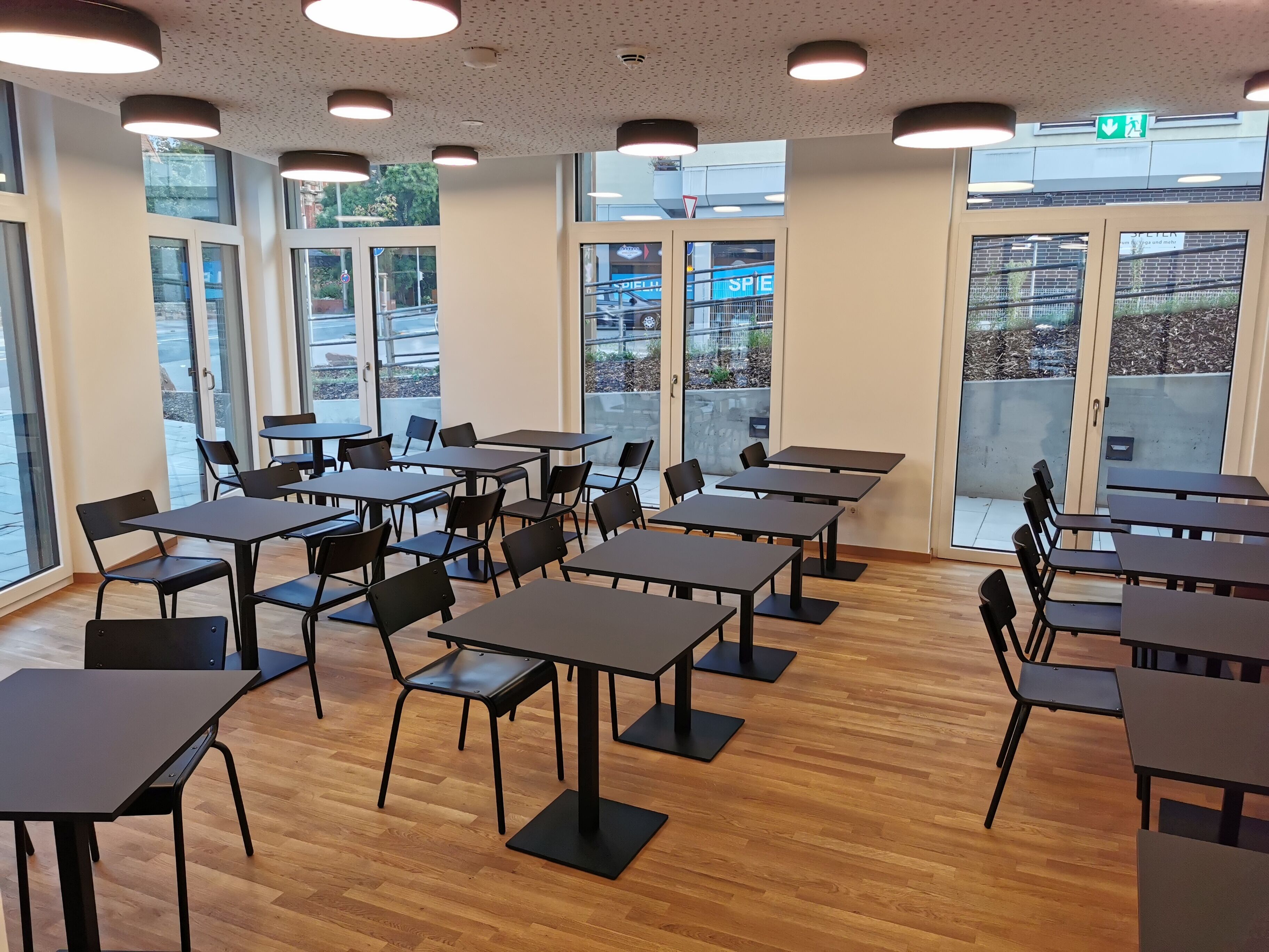 A spacious indoor area with multiple tables and chairs, large windows, and a ceiling with circular lights.