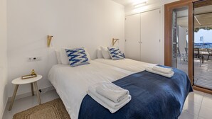 A bedroom with a bed, bedside tables, a mirror, and a view of the sea through a sliding door.