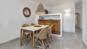 A dining area with a white table and wicker chairs, a wooden cabinet, and a hanging light fixture.