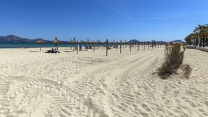 A wide sandy beach with thatched umbrellas and palm trees.