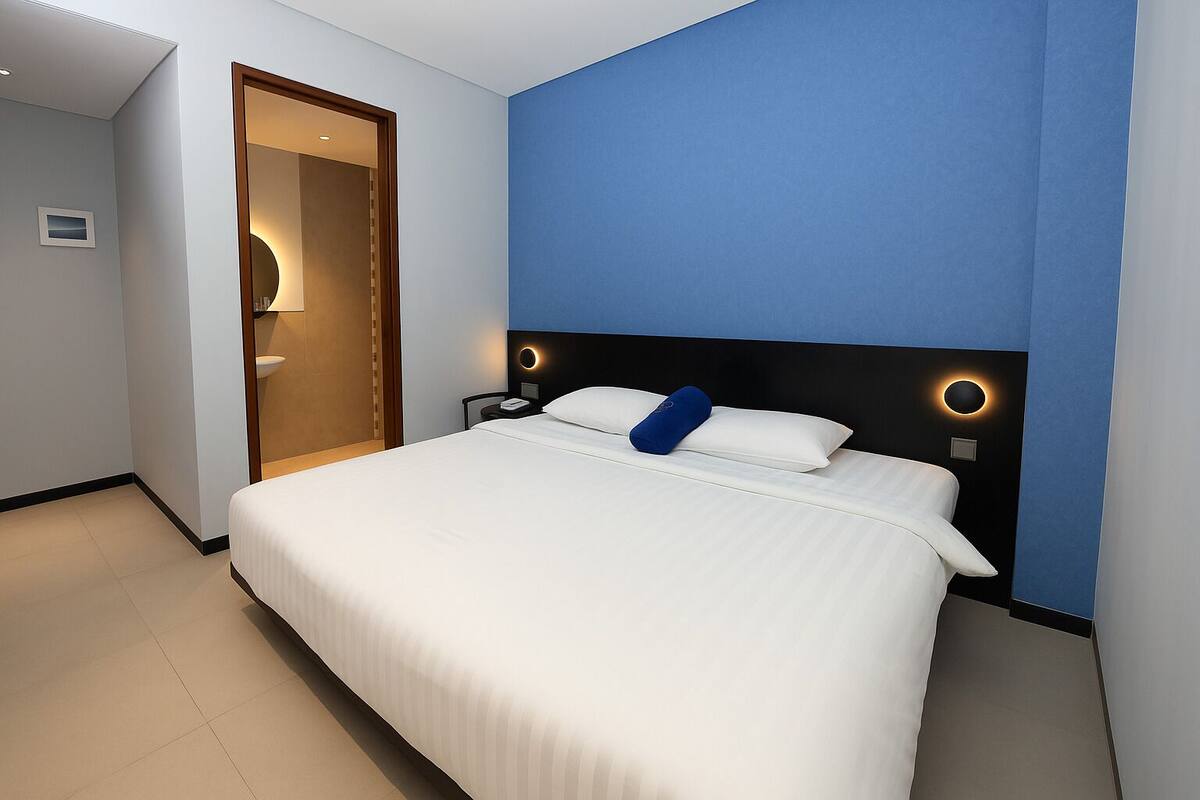 A modern hotel room with a large bed, a bedside table, and a nightstand.