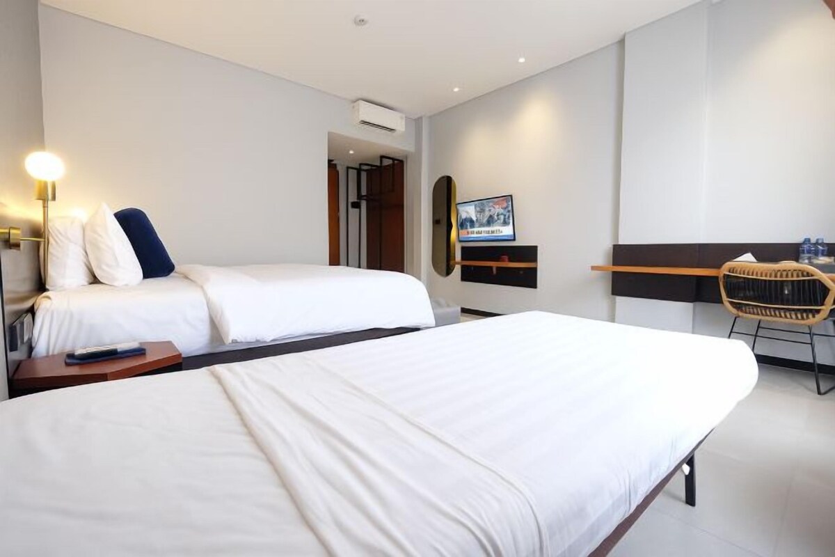 A hotel room with two beds, a desk, a chair, and a TV.